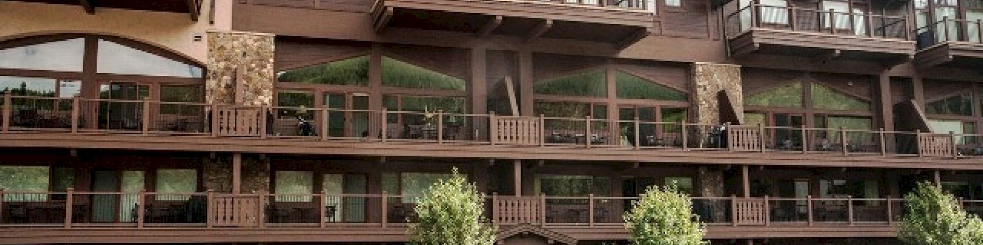 The image shows a multi-story rustic building with wooden balconies and parked cars in front under a partly cloudy sky.