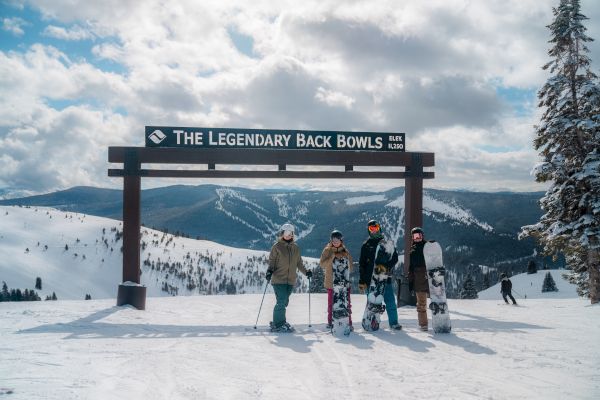 A group of people with snowboards stands under a sign reading 