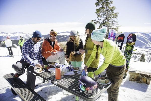 A group of people having a picnic at a snowy location, with ski gear and snowboards nearby.