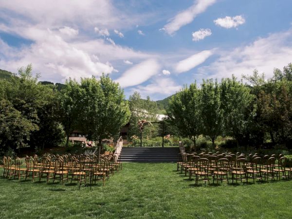 This image shows an outdoor setting with rows of chairs arranged for an event, possibly a wedding, surrounded by lush greenery under a blue sky.