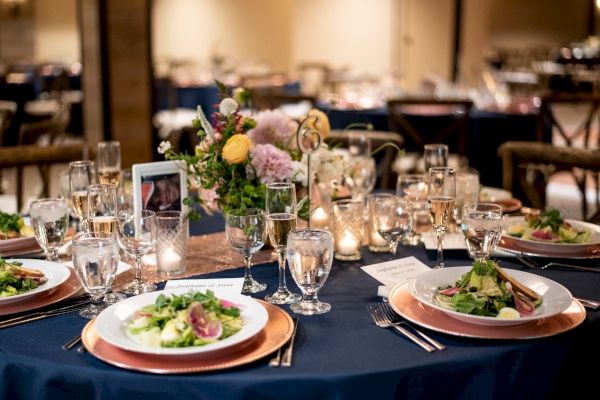 A beautifully set dining table with salads, glassware, flowers, and décor, creating an elegant and inviting atmosphere for a meal.