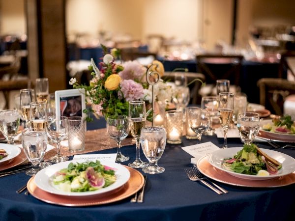 A beautifully set dining table with salads, glassware, flowers, and décor, creating an elegant and inviting atmosphere for a meal.