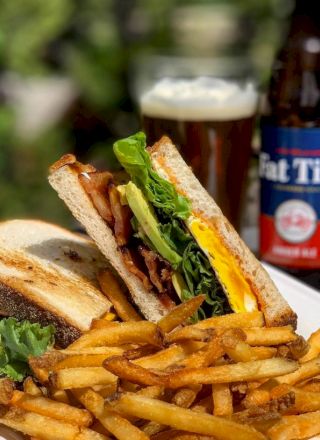 A sandwich with lettuce and cheese, a pile of fries, a glass of beer, and a beer bottle on a table outdoors.