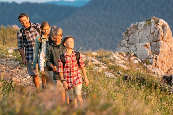 A group of four people hiking on a trail in a mountainous area, smiling and enjoying the outdoors.