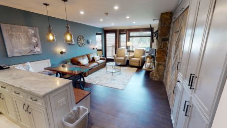 A cozy living room with a couch, armchairs, and a fireplace, connected to a kitchen area with pendant lights and a marble countertop.
