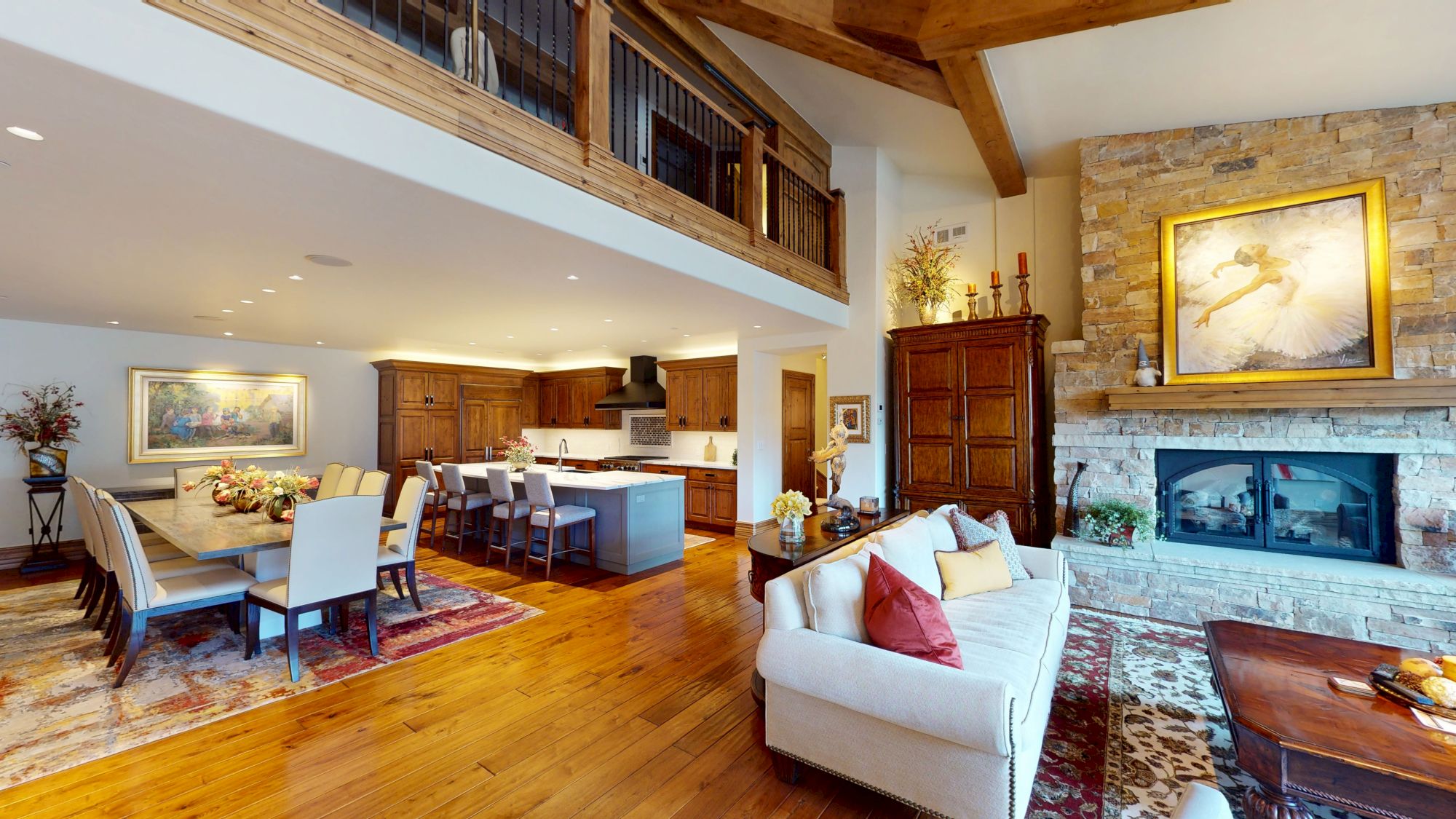 A spacious, open-plan living area with a cozy sofa, dining table, modern kitchen, and stone fireplace under high ceilings.