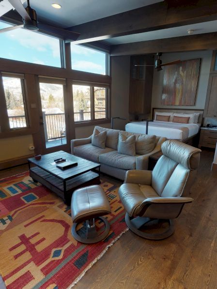 A cozy living space with large windows, modern furniture, and wooden flooring. Colorful rug and barstools accent the room's decor.