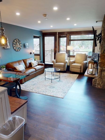 This image shows a modern living area with a kitchen island, pendant lights, a sofa, armchairs, and large windows for natural light.