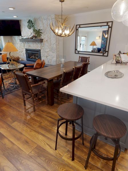 The image shows a modern open-concept kitchen and living area with wooden floors, a kitchen island, and stylish seating and decor.