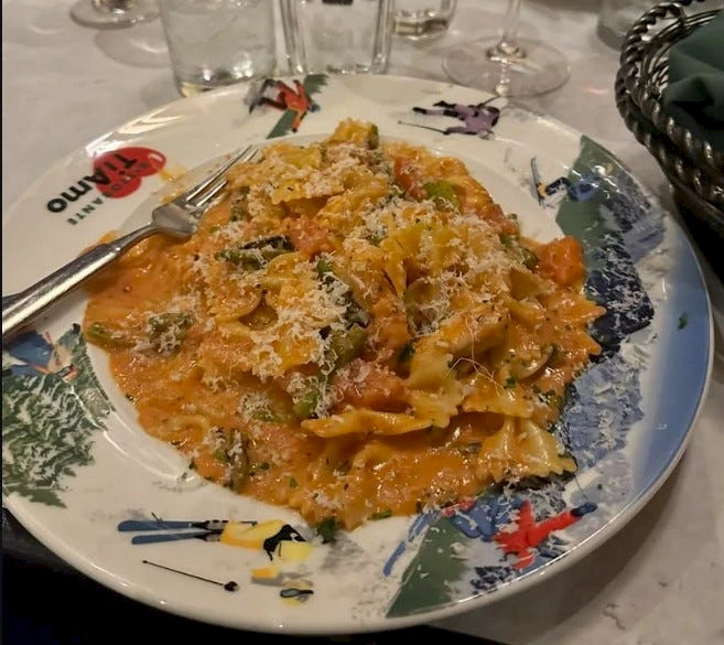 A plate of creamy orange pasta with cheese, herbs, and mushrooms, sprinkled with grated cheese, on a decorative dish with a fork nearby.