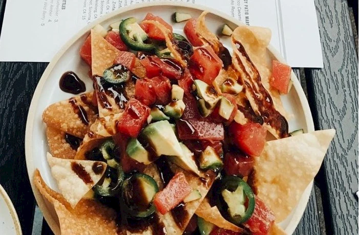 A plate of nachos topped with melted cheese, salsa, guacamole, jalape&ntilde;os, tomatoes, and diced peppers on tortilla chips.