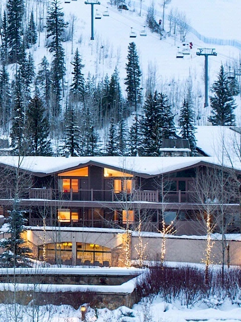 A snowy mountain lodge with warm lights, pine trees, and ski lifts in the background, nestled beside a snow-covered landscape.