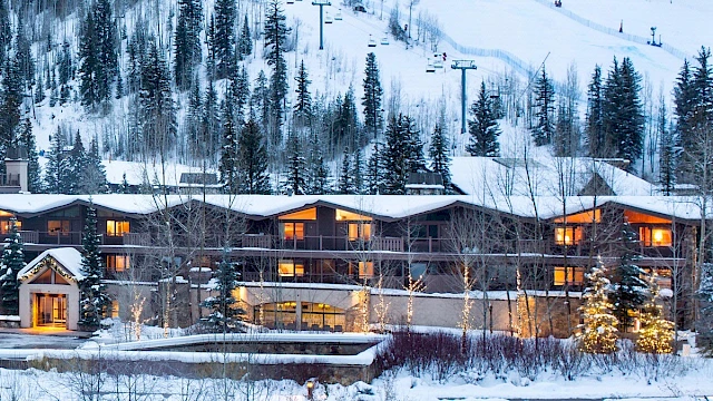 A snowy mountain lodge with warm lights, pine trees, and ski lifts in the background, nestled beside a snow-covered landscape.