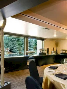 A chic dining room with round table set for a formal meal, warm lighting, a buffet nook, and artistic tree-like dividers by the window.