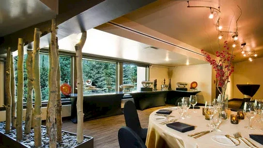 A chic dining room with round table set for a formal meal, warm lighting, a buffet nook, and artistic tree-like dividers by the window.
