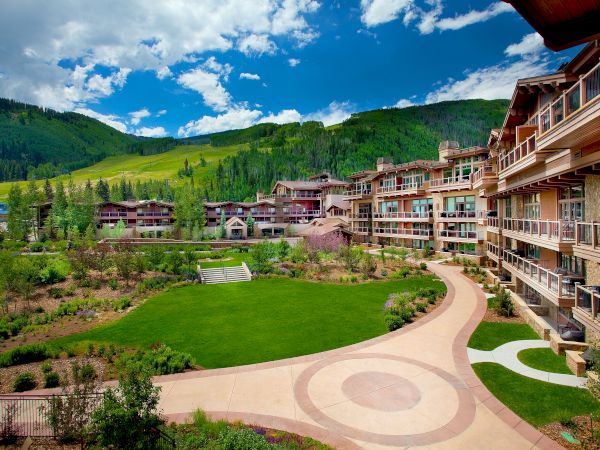 A resort village with green hills, curved walkways, and multi-story lodges surrounding a central lawn.